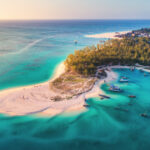 Aerial view of the fishing boats on tropical sea coast with sandy beach at sunset. Summer holiday on Indian Ocean, Zanzibar, Africa. Landscape with boat, green trees, transparent blue water. Top view