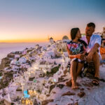 On vacation in Santorini Greece, two men and women visit Oia Santorini with whitewashed buildings. Young couple watching the sunrise in Santorini Greece