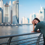 Happy young female traveler in the big city of Dubai, famous place Dubai marina. Luxury and comfortable tourism season in United Arab Emirates.