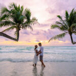 a couple of men and woman watching the sunset on the beach of Koh Kood Island Thailand Trat, tropical beach with palm trees and a turqouse colored ocean, Ko Kut Island