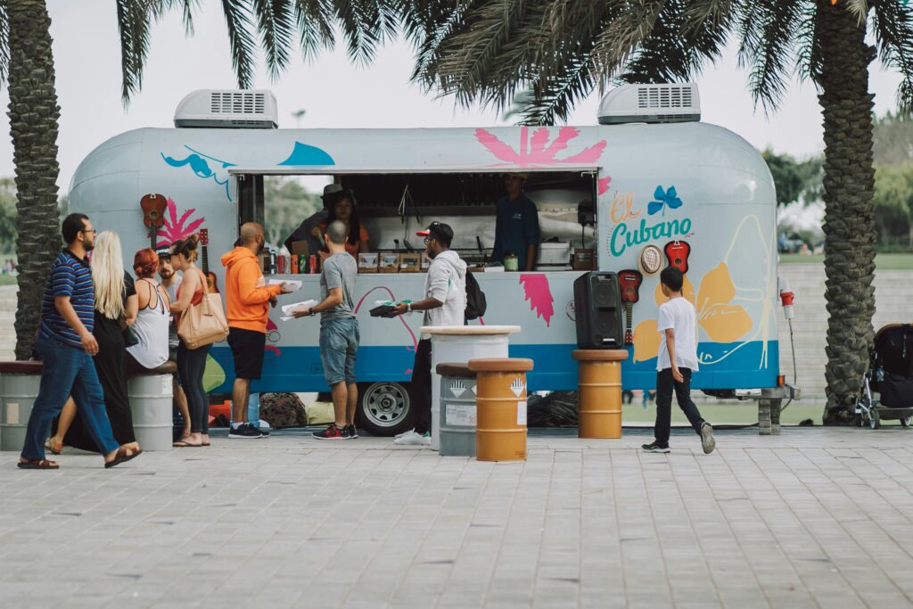 People gather at a colorful food truck, enjoying a lively outdoor setting.