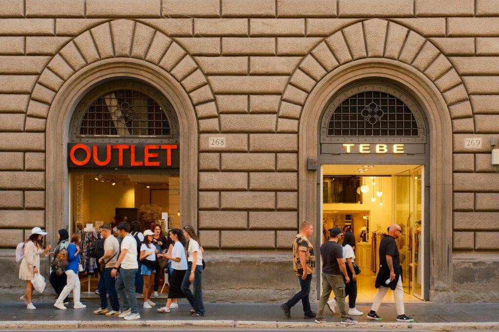 People walking past outlet stores in Florence, Italy under classic architecture.