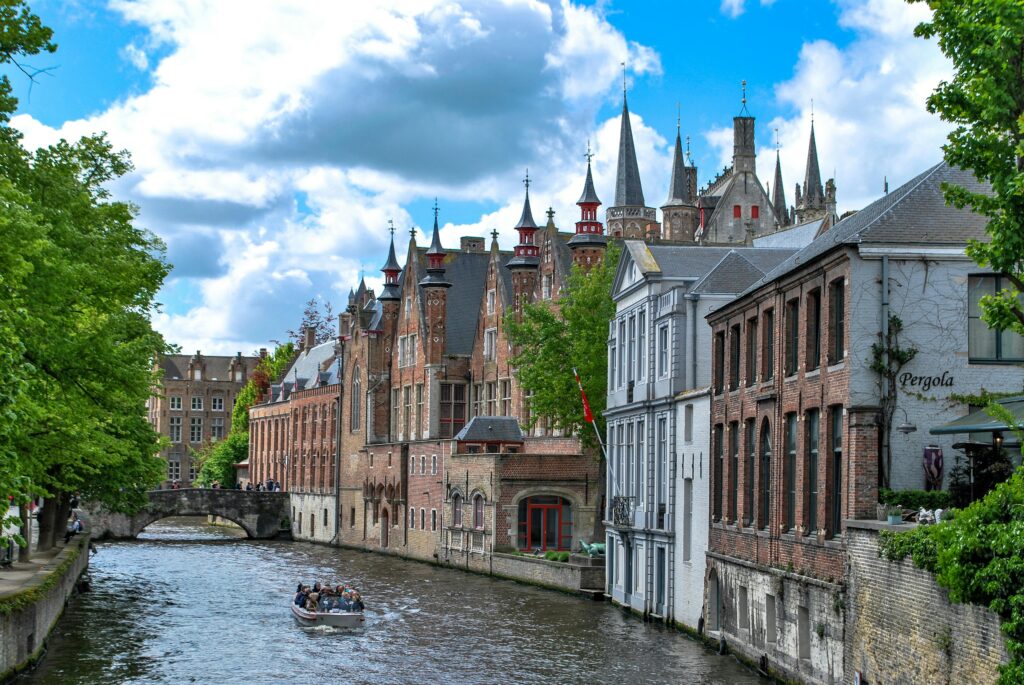 Charming canal scene in Brugge, Belgium showcasing historic architecture and a tour boat on a sunny day.