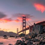 A wide shot of Golden Gate Bridge on the body of water near rock formations during sunset in San Francisco, California