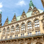 Ornate historic building with classical stone carvings and green roofs, set against a blue sky. A striking example of European architectural heritage.