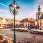 Sunny day in a European city square with historic buildings, street lights and cobblestones.