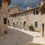 Explore a narrow stone alleyway in a picturesque, sunlit village with rustic architecture.