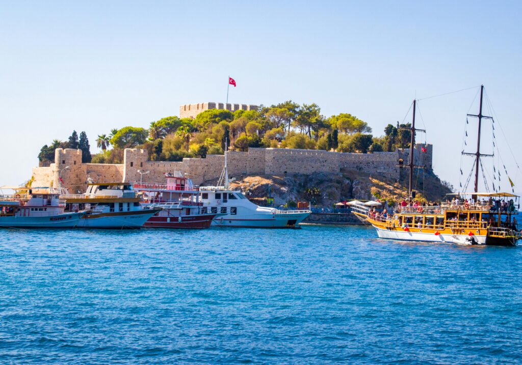 Scenic view of a coastal castle with boats in Kusadasi, Turkey on a clear day.