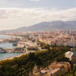 Sunny aerial view of Málaga, capturing its coastline, historic architecture, and mountainous backdrop.