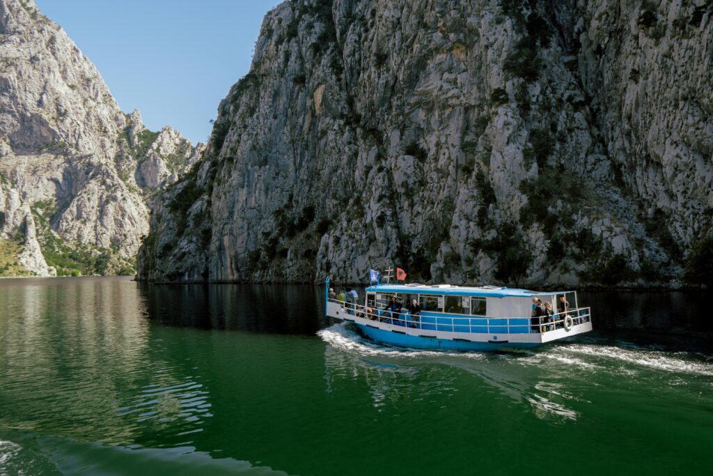 A scenic view of a blue ferry crossing Koman Lake with imposing cliffs in Albania.