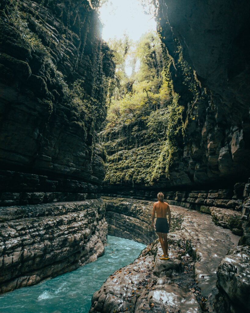 A lone traveler explores a lush green canyon gorge with a flowing river.