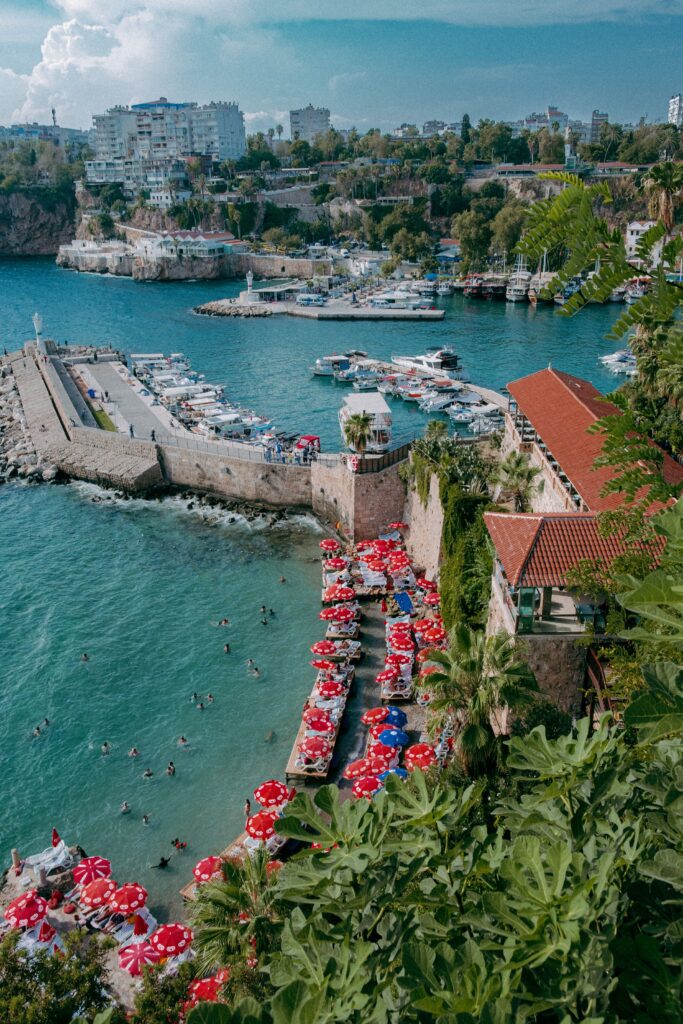 Explore the vibrant coastal scenery of Antalya, Turkey, featuring a bustling marina and shoreline with red umbrellas.