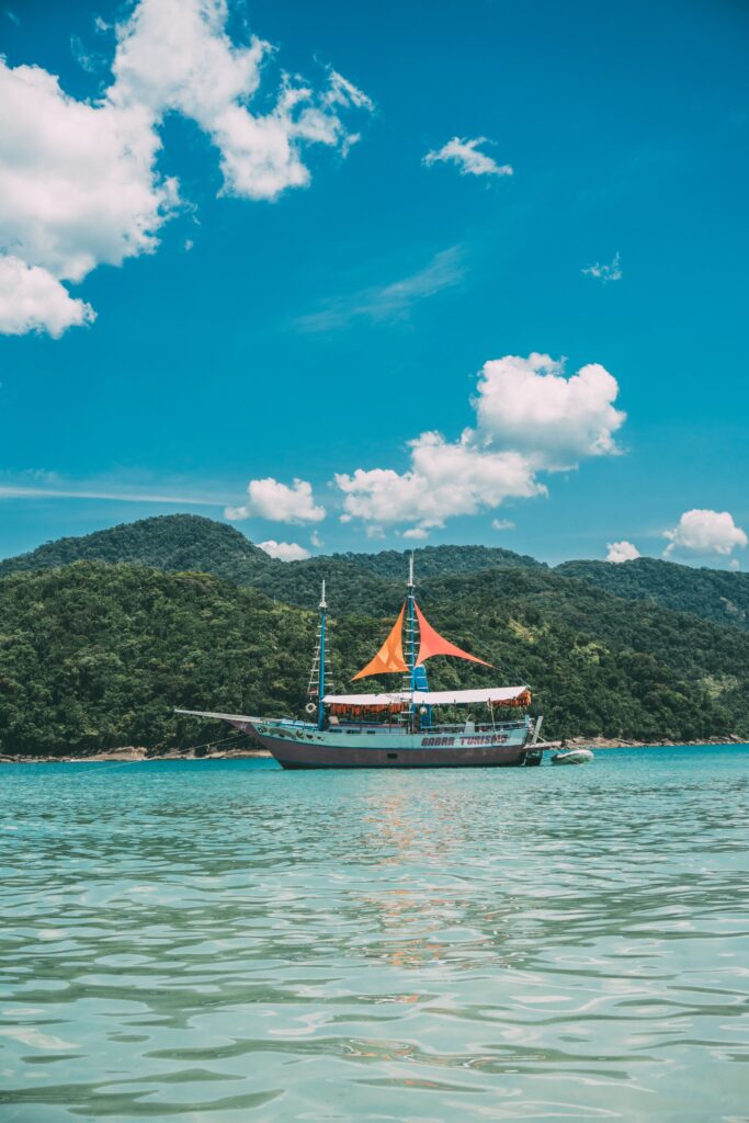 A vibrant cruise ship with colorful sails navigates serene tropical waters under deep blue skies.