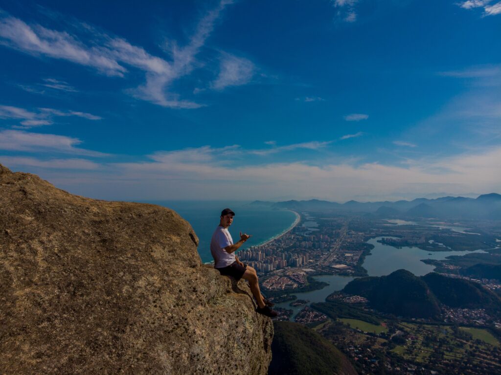Man enjoying stunning Rio de Janeiro view from Pedra da Gávea cliff. Perfect for travel and adventure enthusiasts.