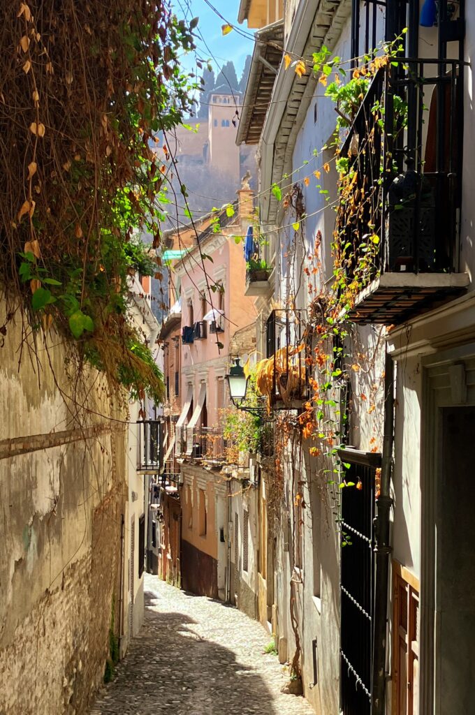 Sunlit narrow alley in Granada, Spain, with a view of the Alhambra palace.