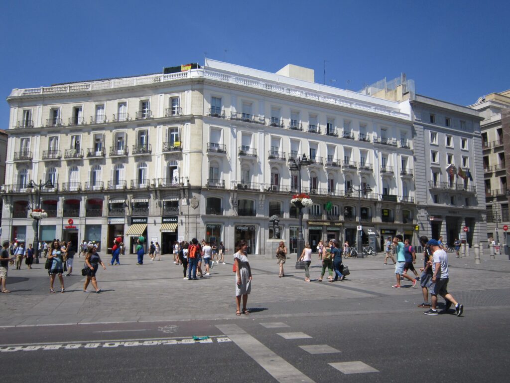 A vibrant scene at Puerta del Sol in Madrid featuring pedestrians on a bright summer day.