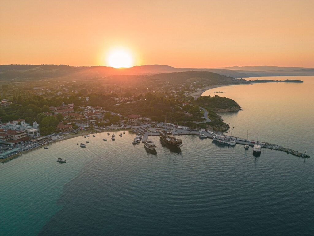 Aerial view of a picturesque coastal harbor at sunset with boats and calm waters.