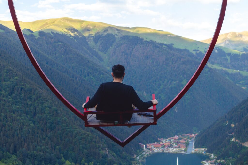 Man on swing overlooking Uzungöl Lake and lush mountains in Trabzon, Turkey.
