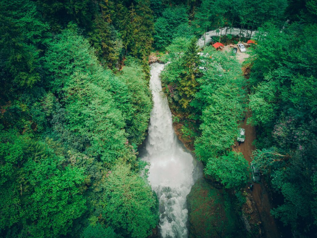 Drone shot capturing a waterfall cascading through dense green forest, offering a stunning natural view.