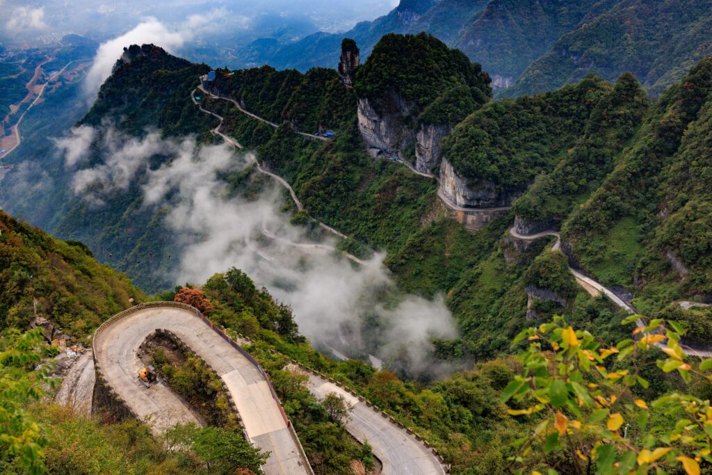Breathtaking view of a winding road in Tianmen Mountain with lush green landscape and misty clouds.